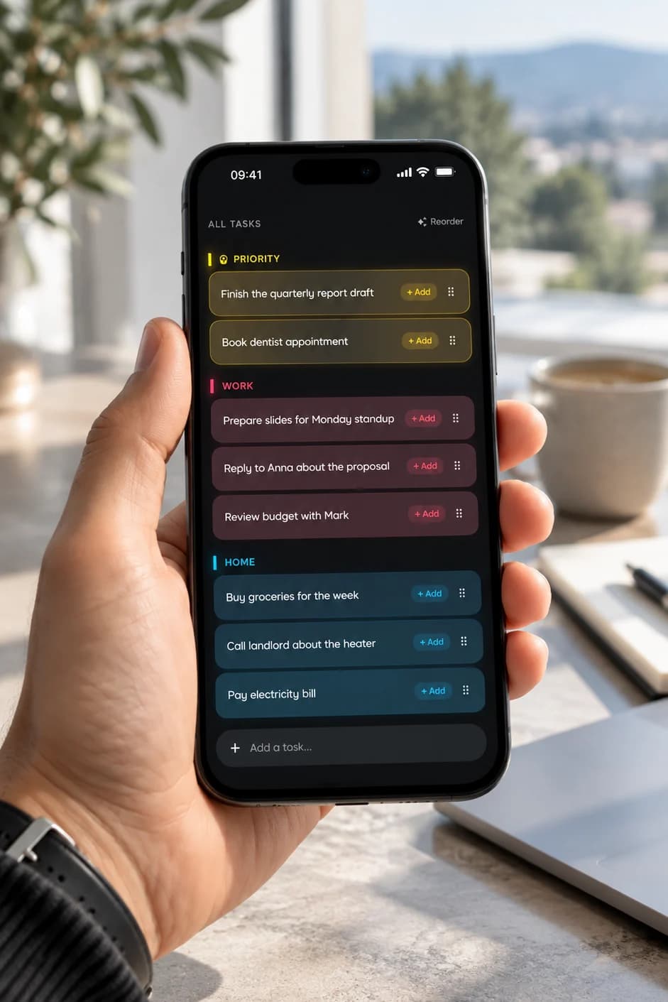 A hand holding an iPhone showing Podomodo tasks sorted into Priority, Work and Home, at a sunny desk
